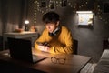 Young guy student studying at the college dormitory, sitting at the desk, using laptop computer, holding mobile phone. Royalty Free Stock Photo