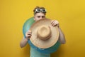 young guy in the summer on vacation with an inflatable swimming circle is shy and hides behind a big straw hat Royalty Free Stock Photo