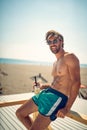 A young guy in swimsuite is sitting on the beach and posing for a photo. Summer, beach, sea Royalty Free Stock Photo