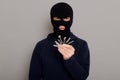 A young guy thief holds stolen keys from house or other property in his hands, wearing hoodie and robber mask, looks at camera,