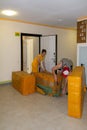 A young guy unpacks large yellow parcels from China in an inter-apartment hall, and a young beautiful girl in a yellow dress helps