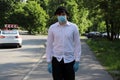 A young guy walks down the street on a summer day in a white shirt and a mask on his face. Mask mode.