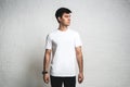 Young guy wearing white blank t-shirt, horizontal studio portrait, empty wall