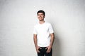 Young guy in white blank t-shirt, horizontal studio portrait. White wall