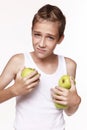 A young guy in a white shirt, holds two apples in one hand, and wipes an apple against the shirt with the other hand. Royalty Free Stock Photo