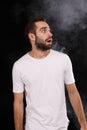 A young guy in a white T-shirt on a black background with smoke looks to the side Royalty Free Stock Photo