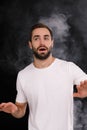 A young guy in a white T-shirt on a black background with smoke looks to the side Royalty Free Stock Photo