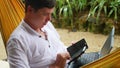 Young guy working on laptop and smartphone lying in a hammock