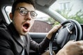 Young guy yawns while looking at the camera. He is sitting at his car. His hands are on the steering wheel Royalty Free Stock Photo