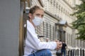 A young guy 20-25 years old in a medical mask with a backpack is sitting on the steps at the entrance to the building. Closed entr Royalty Free Stock Photo