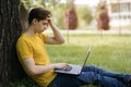 A young guy in a yellow T-shirt sits on the lawn and works hard with a laptop Royalty Free Stock Photo