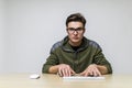 Young hacker with glasses dressed in casual clothes sitting at a desk and working on a computer keyboard in front Royalty Free Stock Photo