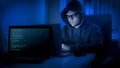 Portrait of young hacker sitting in dark room and working on laptop