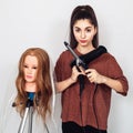 Young hairdresser with a curling iron, hair dryer and a mannequin head on a tripod. Royalty Free Stock Photo