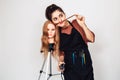 Young hairdresser with a curling iron and a mannequin head on a tripod. The girl makes a mustache out of hair. Royalty Free Stock Photo