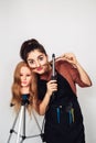 Young hairdresser with a curling iron and a mannequin head on a tripod. The girl makes a mustache out of hair. Royalty Free Stock Photo