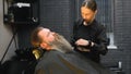 a young hairdresser girl serves a client by combing his beard from a beauty salon.