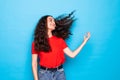 Young haired curly woma playing with hair standing over blue background