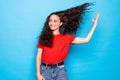 Young haired curly woma playing with hair standing over blue background