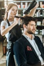 Young hairstylist combing and drying hair to handsome client