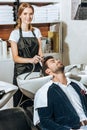 Young hairstylist smiling at camera while washing hair to handsome young male client Royalty Free Stock Photo