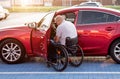 Young handicapped driver getting in red car fom wheelchair