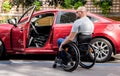 Young handicapped driver getting in red car fom wheelchair