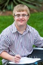 Young handicapped student writing in file outdoors.