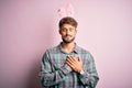 Young handsome adult man wearing cute easter rabbit ears over pink isolated background smiling with hands on chest with closed Royalty Free Stock Photo