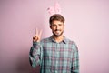 Young handsome adult man wearing cute easter rabbit ears over pink isolated background smiling with happy face winking at the Royalty Free Stock Photo