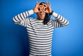 Young handsome african american afro man with dreadlocks wearing casual striped sweater doing ok gesture like binoculars sticking Royalty Free Stock Photo