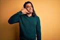 Young handsome african american afro man with dreadlocks wearing green casual sweater smiling doing phone gesture with hand and Royalty Free Stock Photo