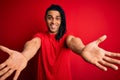 Young handsome african american afro man with dreadlocks wearing red casual t-shirt looking at the camera smiling with open arms Royalty Free Stock Photo