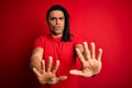 Young handsome african american afro man with dreadlocks wearing red casual t-shirt Moving away hands palms showing refusal and