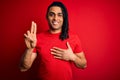 Young handsome african american afro man with dreadlocks wearing red casual t-shirt smiling swearing with hand on chest and Royalty Free Stock Photo