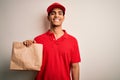 Young handsome african american delivery man holding paper bag with takeaway food with a happy face standing and smiling with a Royalty Free Stock Photo