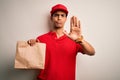 Young handsome african american delivery man holding paper bag with takeaway food with open hand doing stop sign with serious and Royalty Free Stock Photo