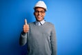 Young handsome african american engineer man with dreadlocks wearing safety helmet doing happy thumbs up gesture with hand Royalty Free Stock Photo