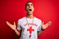 Young handsome african american lifeguard man wearing t-shirt with red cross and whistle crazy and mad shouting and yelling with