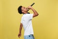Young handsome African American Male Singer Performing with Microphone. Isolated over yellow gold background. Royalty Free Stock Photo