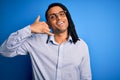 Young handsome african american man with dreadlocks wearing casual shirt and glasses smiling doing phone gesture with hand and Royalty Free Stock Photo