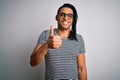 Young handsome african american man with dreadlocks wearing striped t-shirt and glasses doing happy thumbs up gesture with hand Royalty Free Stock Photo