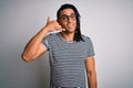 Young handsome african american man with dreadlocks wearing striped t-shirt and glasses smiling doing phone gesture with hand and Royalty Free Stock Photo
