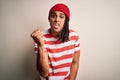 Young handsome african american man with dreadlocks wearing striped t-shirt and wool hat angry and mad raising fist frustrated and Royalty Free Stock Photo