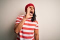 Young handsome african american man with dreadlocks wearing striped t-shirt and wool hat shouting and screaming loud to side with Royalty Free Stock Photo