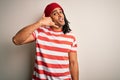 Young handsome african american man with dreadlocks wearing striped t-shirt and wool hat smiling doing phone gesture with hand and Royalty Free Stock Photo