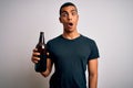 Young handsome african american man drinking bottle of beer over white background scared in shock with a surprise face, afraid and Royalty Free Stock Photo