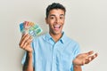 Young handsome african american man holding australian dollars celebrating achievement with happy smile and winner expression with Royalty Free Stock Photo