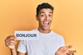 Young handsome african american man holding bonjour french greeting word celebrating achievement with happy smile and winner