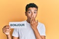 Young handsome african american man holding bonjour french greeting word covering mouth with hand, shocked and afraid for mistake